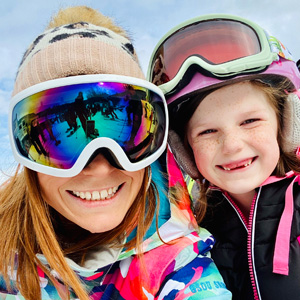 Smiling woman with ski goggles beside smiling child