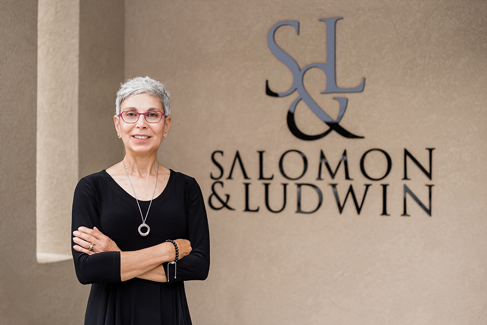 Dalal Salomon standing in front of large S&L Salomon and Ludwin logo.