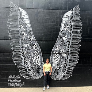 Abbey standing in front of mural depicting large wings with geometric pattern