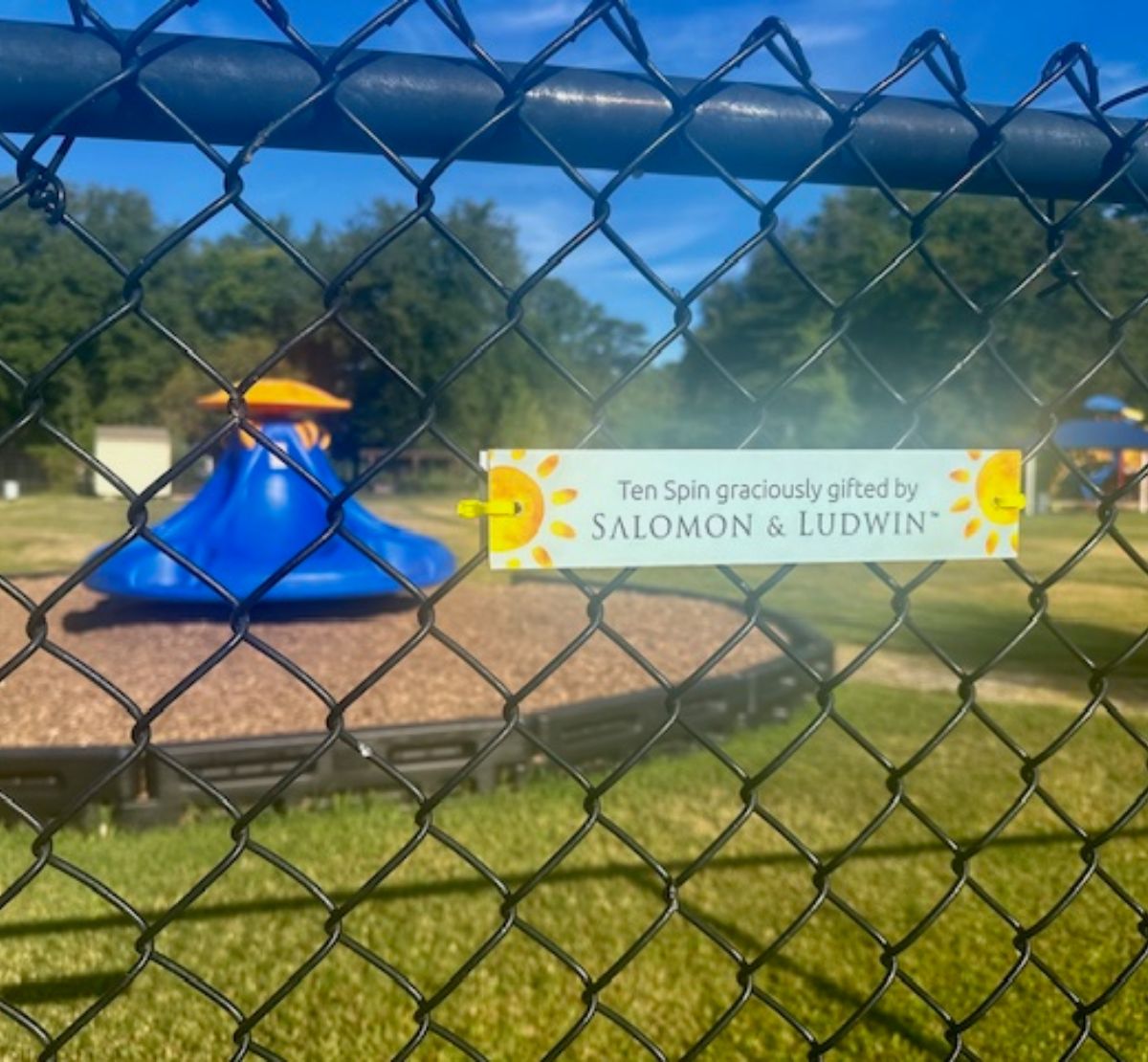 Playground behind a fence with a sign that reads "Ten Spin graciously gifted by Salomon & Ludwin"